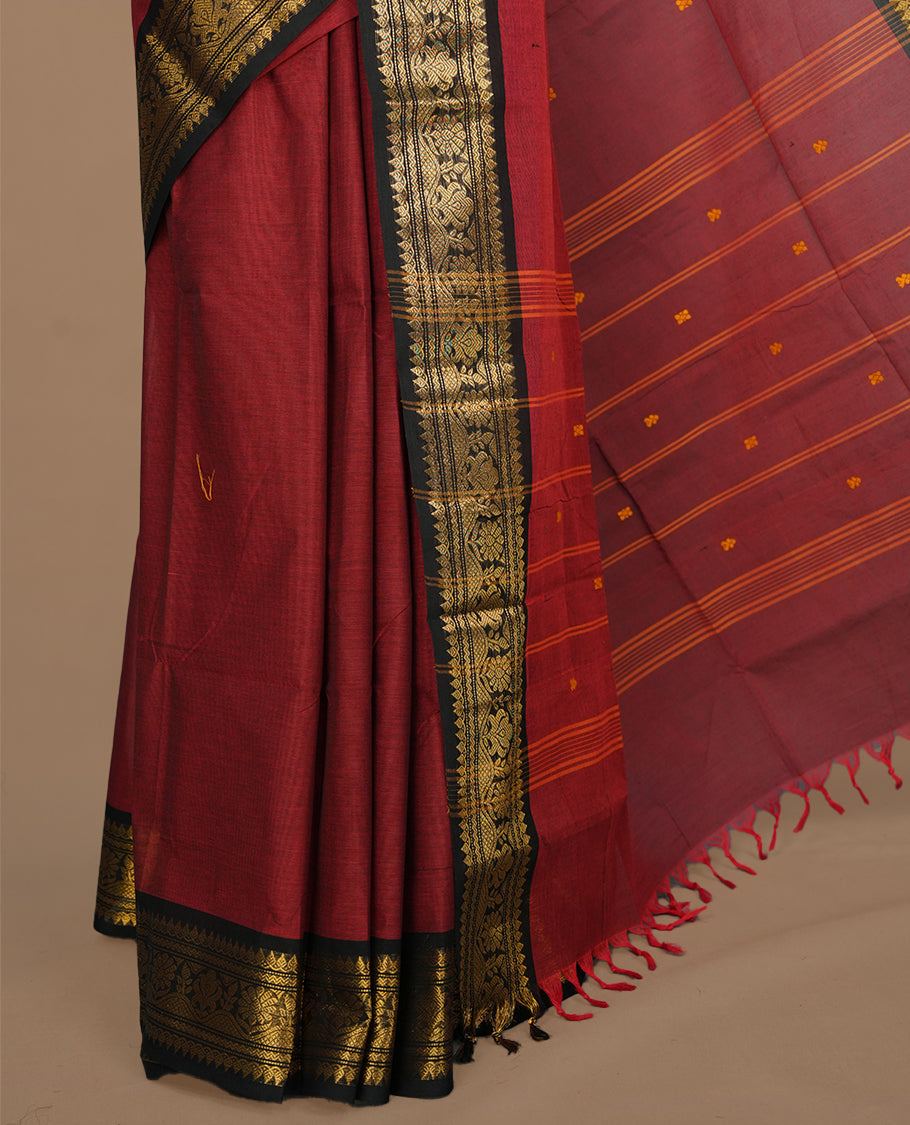 Maroon colour chettinad saree featuring gold zari motifs on body, complemented by contrast black colour with traditional border, paired with matching blouse piece.