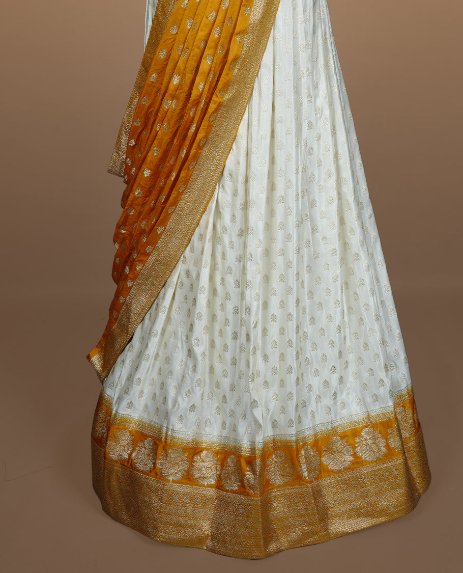 Off white semi banaras semi stitched dhavani set featuring gold zari motifs and contrast Yellow colour and traditional border, unstitched gold zari blouse piece and matching Duptta.