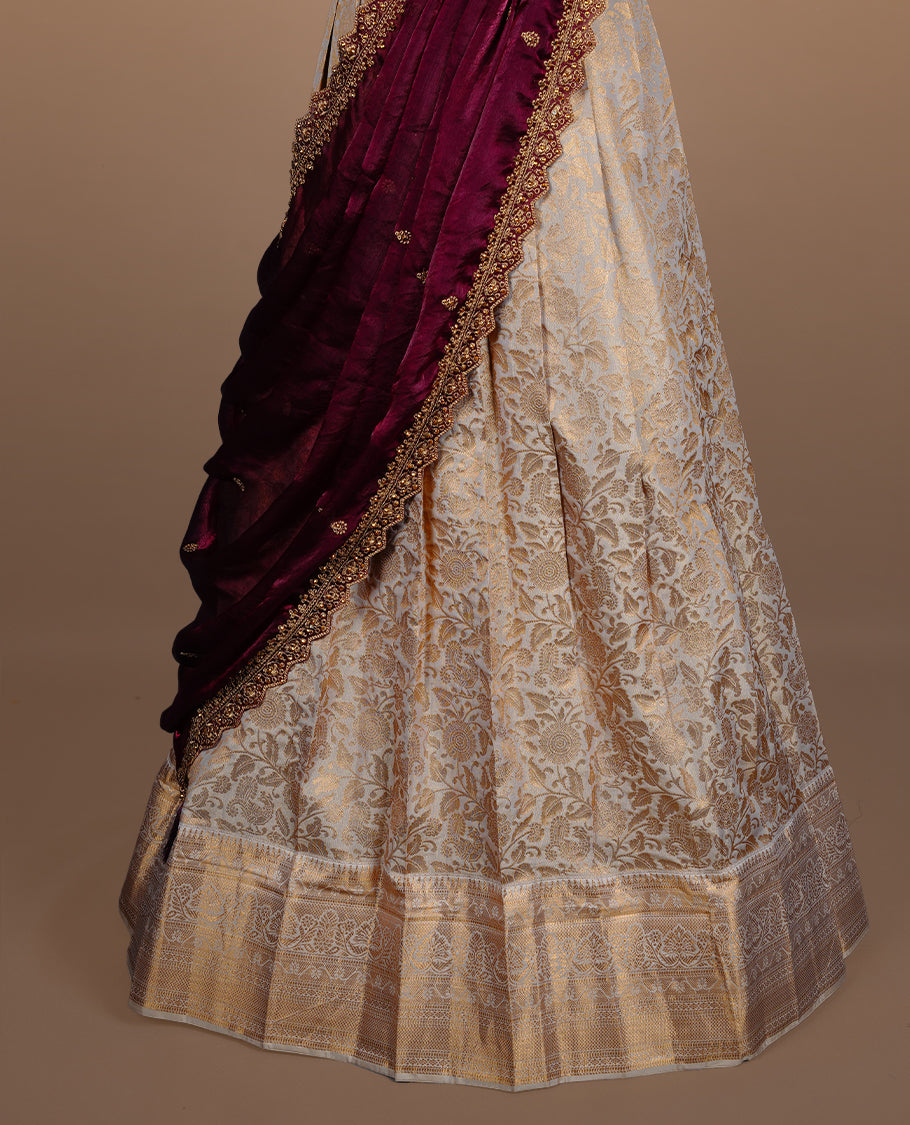 Light gold colour semi banaras semi stitched dhavani set featuring gold zari floral kodi motifs and traditional border, unstitched matching blouse piece and contrast Maroon colour Duptta with gold thread and beats worked border.