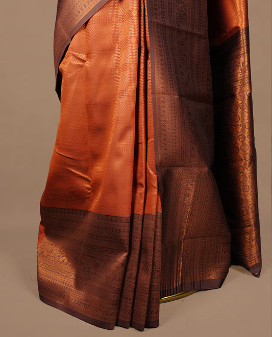 Burnt orange colour silk saree featuring gold zari check and motifs on body, complemented by contrast chocolate with traditional border, paired with matching blouse piece.