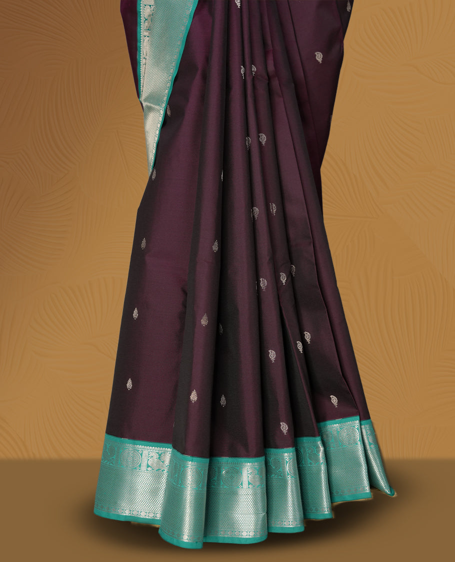 Deep plum colour body soft silk saree adorned with silver buttas, paired with a contrasting light aqua green zari border & Comes with a matching blouse.