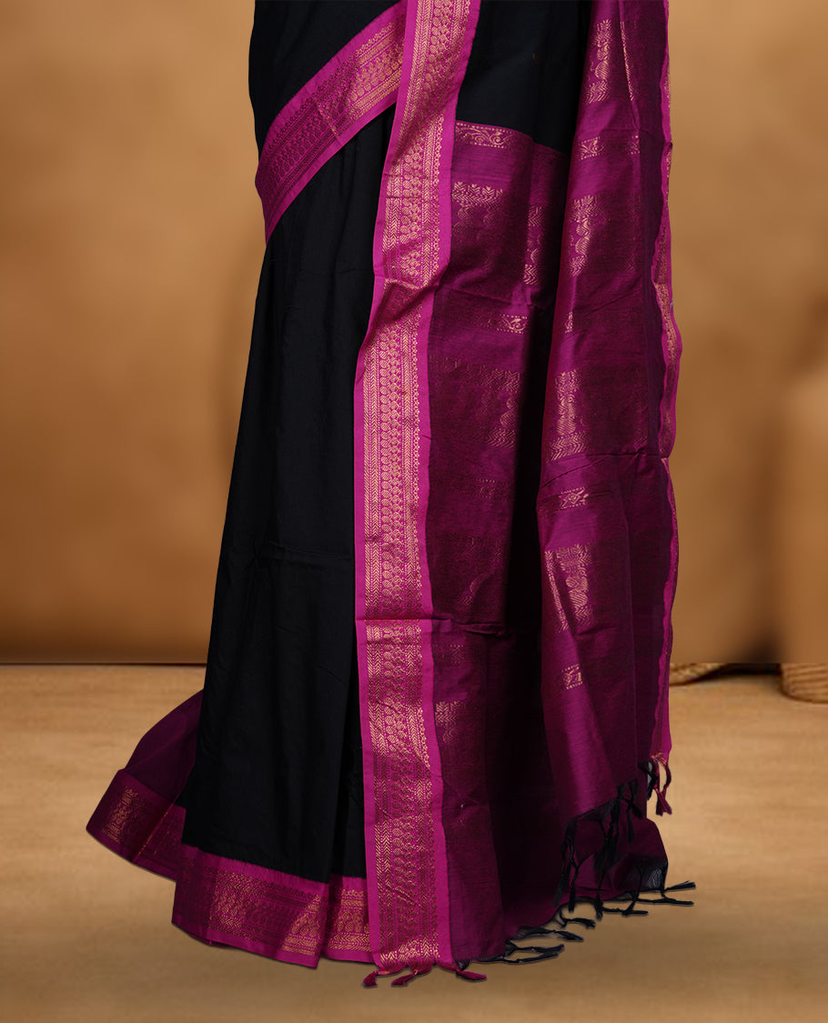 Black colour Kalyani cotton saree featuring delicate zari buttas on the body, complemented by a magenta zari border and woven pallu, paired with a matching blouse.