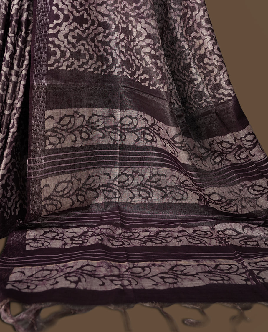 Chocolate colour semi jute tissue saree featuring intricate wave motifs all over the body, enhanced with a shimmering zari striped pallu, woven border, and matching blouse piece.