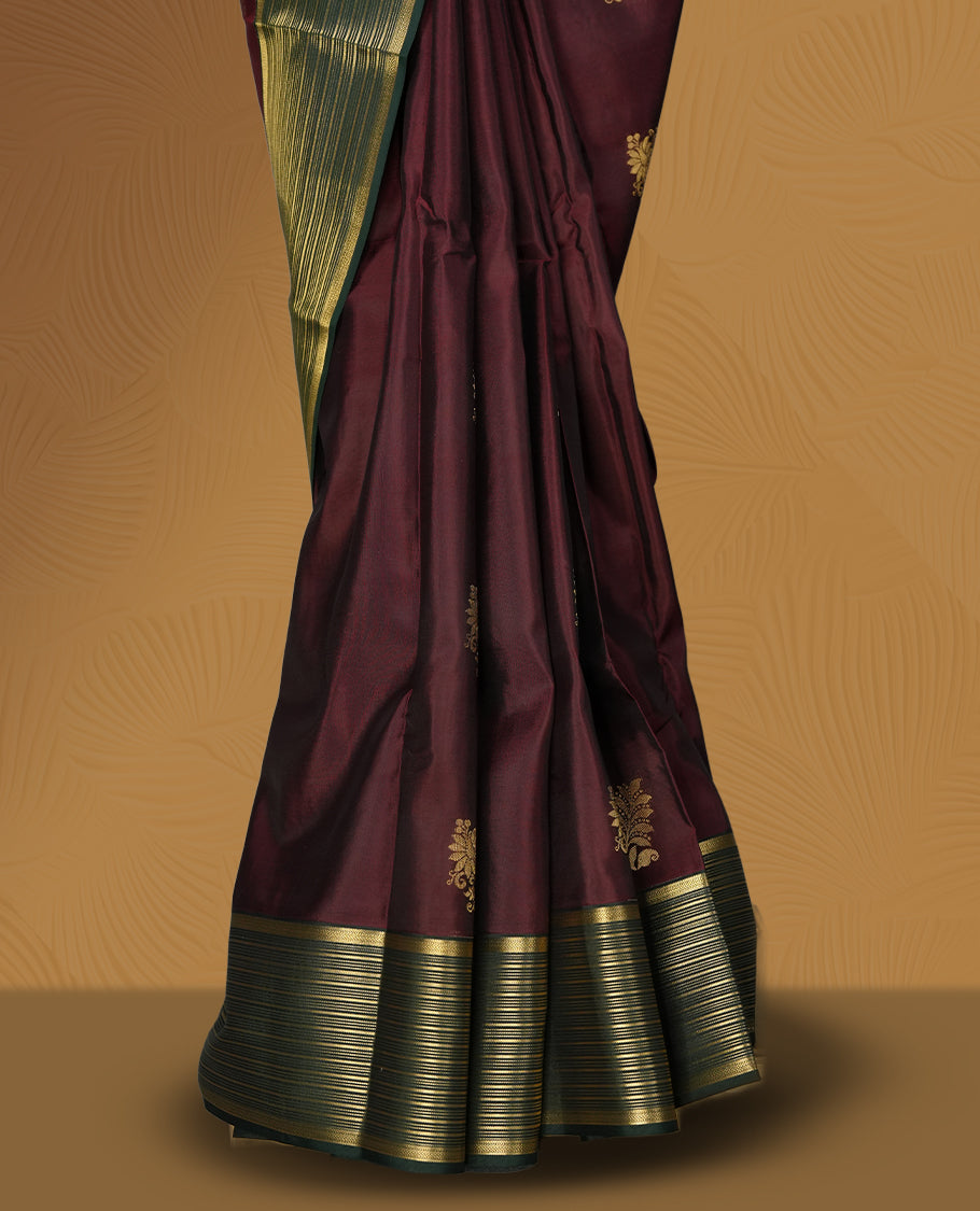 Deep maroon colour soft silk saree adorned with golden buttas, enhanced by a striking green zari border and pallu with intricate designs & Paired with a matching blouse.