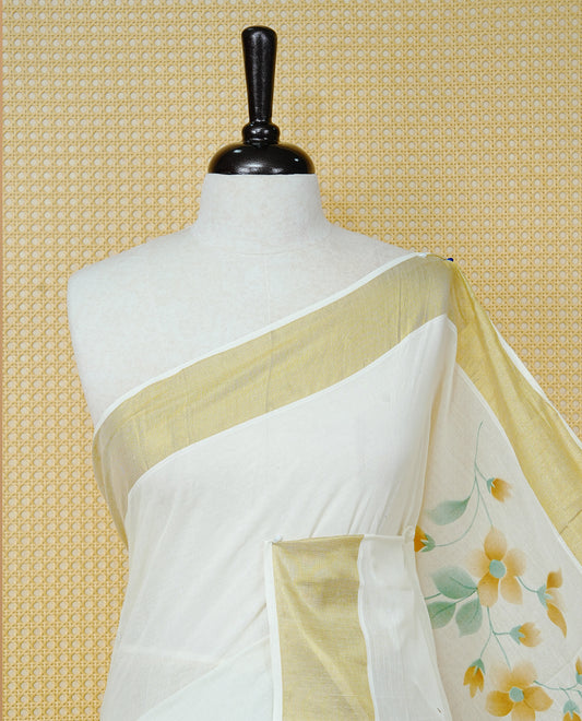 Cream Colour Cotton Kerala Saree Featuring Digital Floral Prints Across The Body, Enhanced With A Gold Zari Border, Traditional Gold Zari Pallu, Finished With Light Brown & White Tassels And A Matching Blouse Piece.