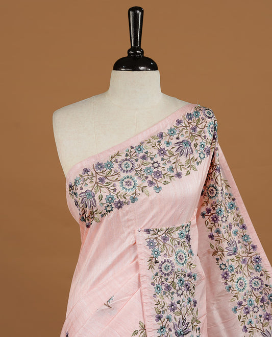 Pastel pink colour Semi Tussar silk saree features an intricate, multi colored Kashmiri Kashida style floral embroidered border and scattered motifs, paired with a matching unstitched blouse piece.