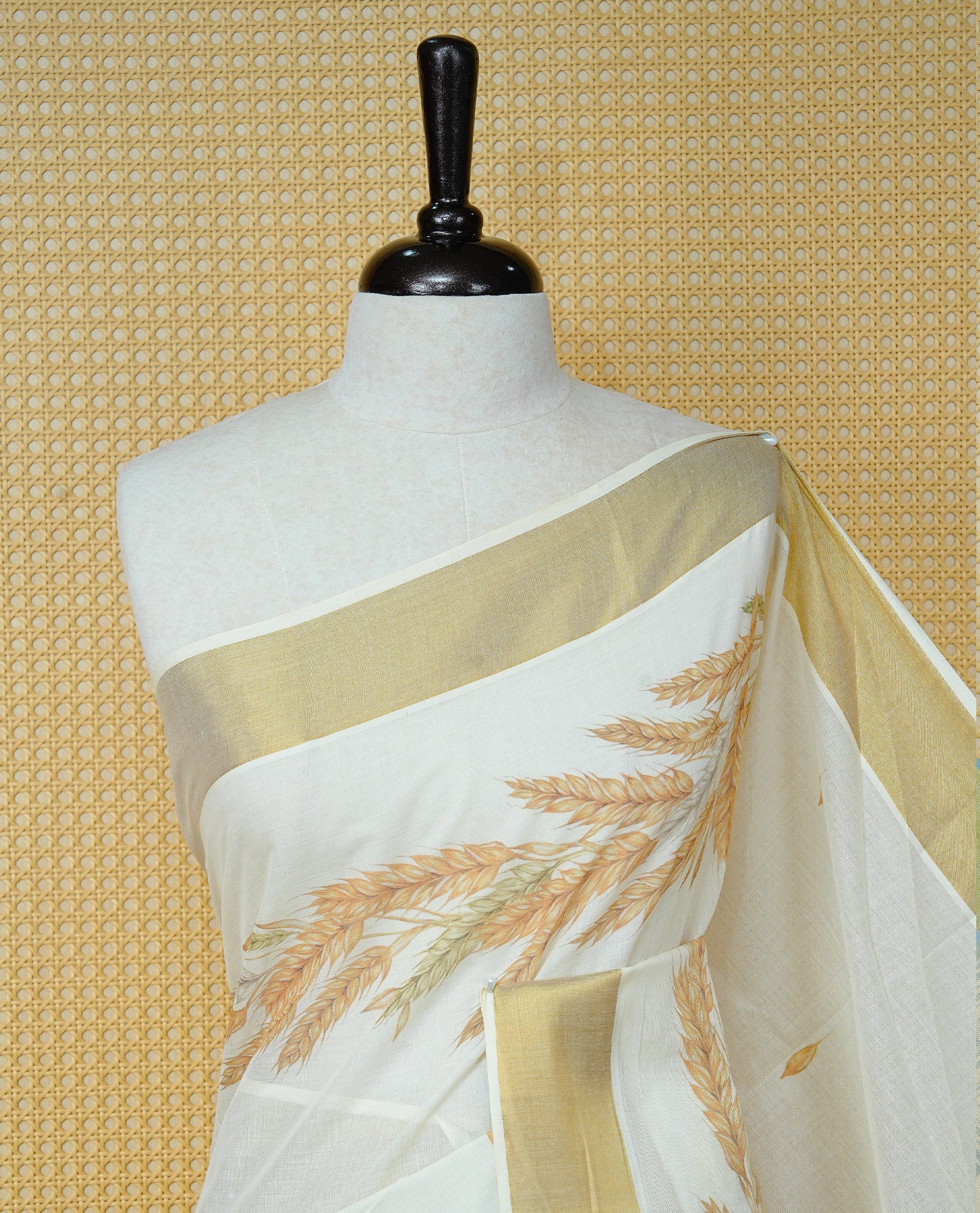 Cream Colour Cotton Kerala Saree Featuring Delicate Wheat Motifs and Scattered Leaf Designs On Body, Enhanced with a Classic Gold Zari Border. The Pallu Is Finished with Light Green Tassels and Paired with a Matching Blouse Piece.