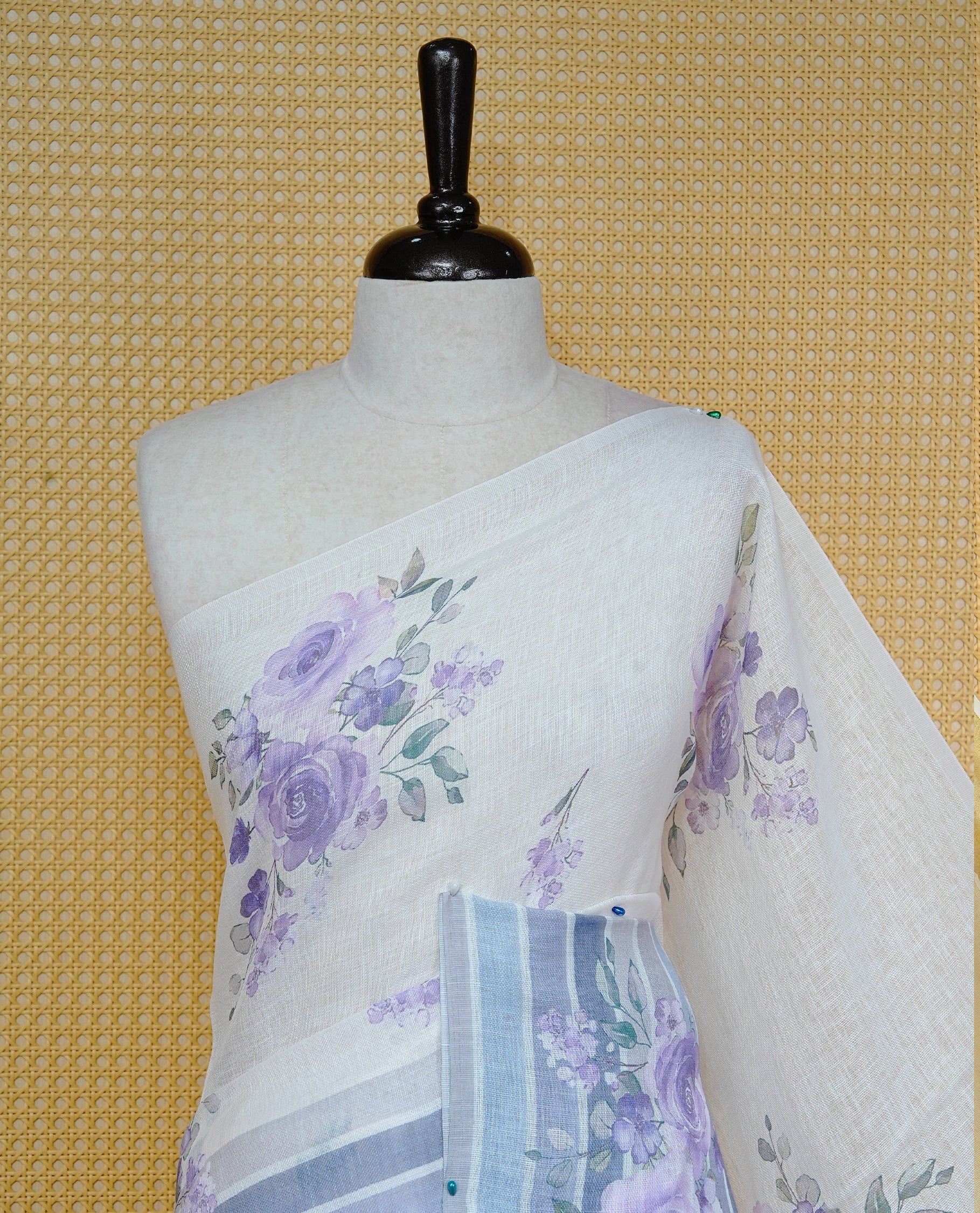 Cream colour semi linen saree featuring Purple colour floral print on body, complemented by contrast Strip pattern border, comes with matching blouse piece.