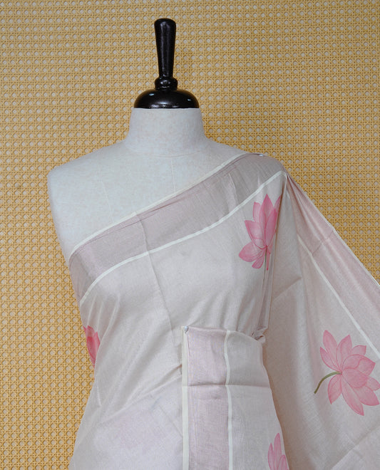 Cream Colour Tissue Kerala Saree Featuring Delicate Digital Lotus Prints And A Charming Cow & Calf Pallu, Enhanced With A Subtle Tissue Border And Contrast Pink Tassels. Paired With A Matching Blouse Piece.