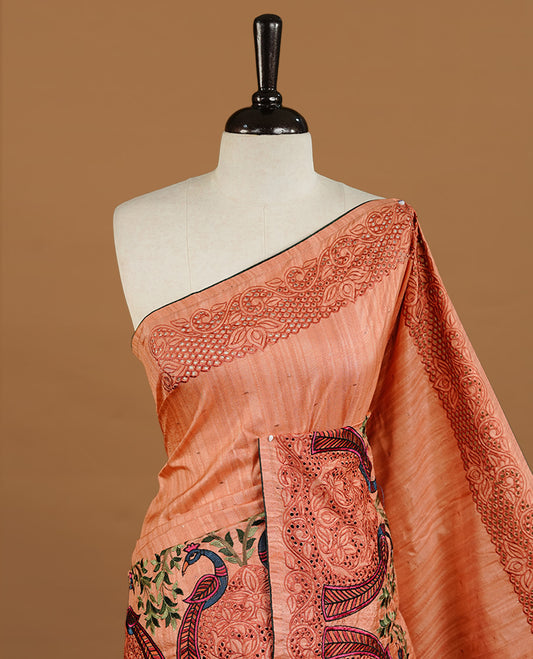 Peach colour Semi Tussar silk saree features an intricate cutwork embroidered peacock motifs on border, paired with a matching unstitched blouse piece.