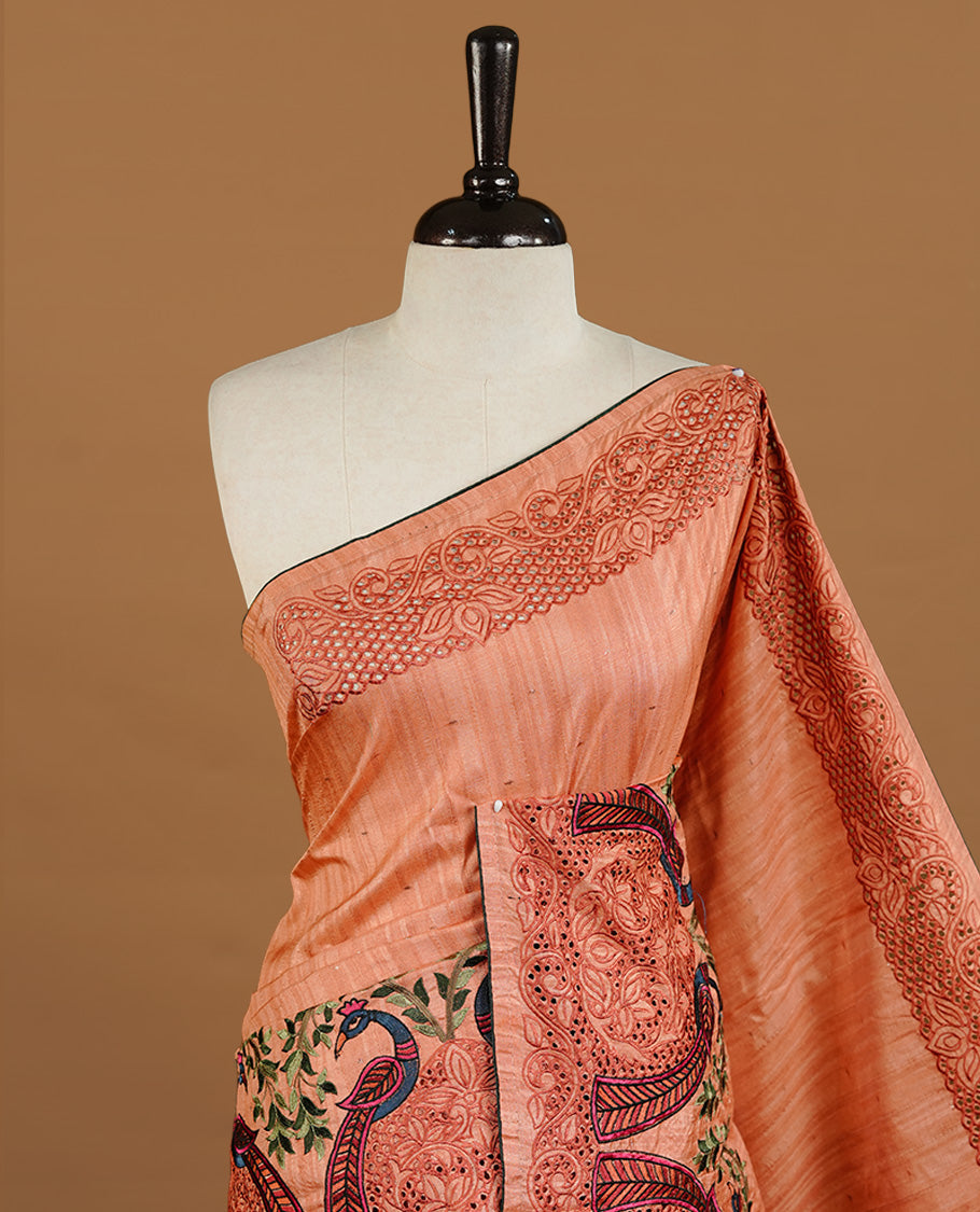 Peach colour Semi Tussar silk saree features an intricate cutwork embroidered peacock motifs on border, paired with a matching unstitched blouse piece.