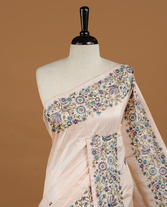 Pastel Peach colour Semi Tussar silk saree features an intricate, multi colored Kashmiri Kashida style floral embroidered border and scattered motifs, paired with a matching unstitched blouse piece.