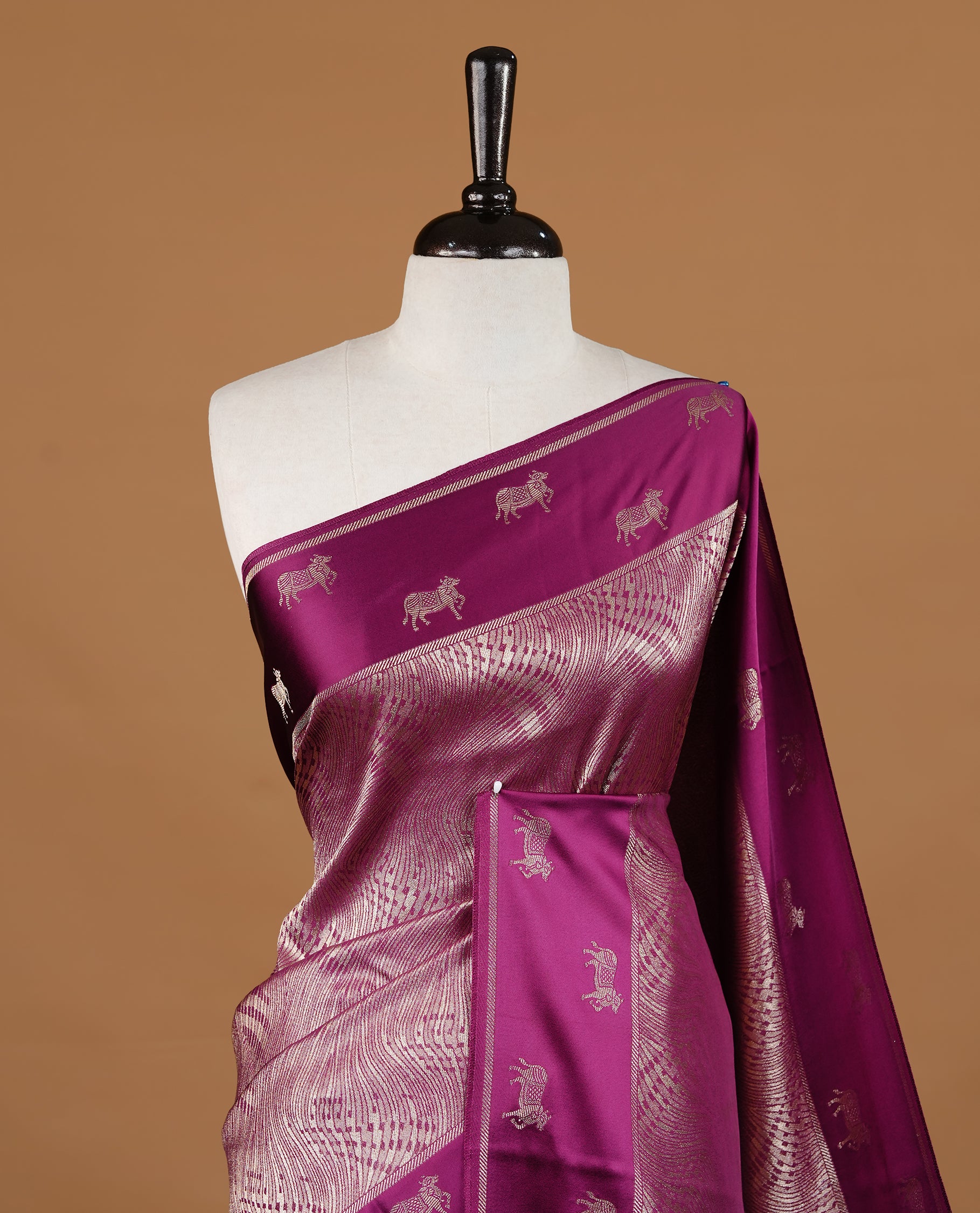 Burgundy colour semi Banaras crepe silk saree featuring an elegant gold zari patterned body, highlighted by a plain border adorned with traditional gold zari cow motifs. Paired with a matching blouse piece.