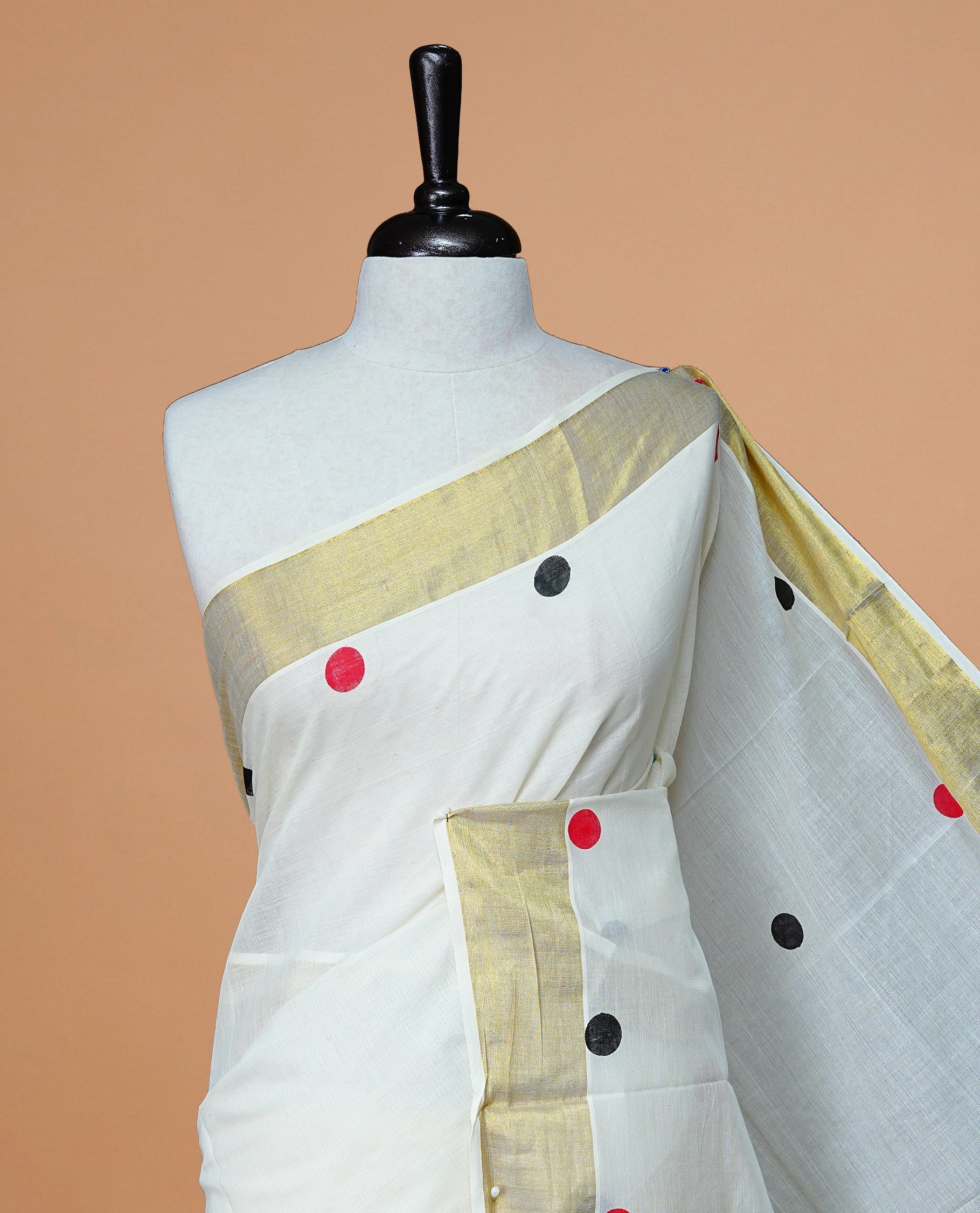 Cream Colour cotton Kerala Saree Featuring  Black & Red Dot Prints On The Body, Complemented By A Traditional Gold Zari Border, Paired With A Matching Blouse Piece.
