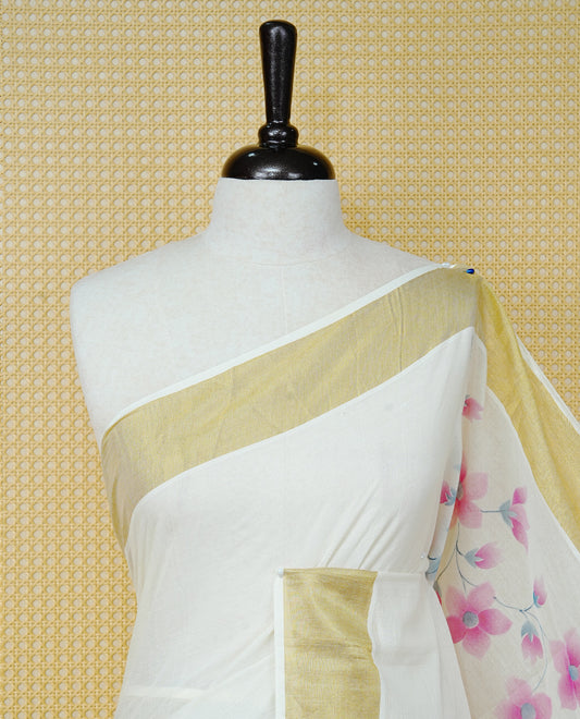 Cream Colour Cotton Kerala Saree Featuring Digital Pink Floral Prints Across The Body, Enhanced With A Gold Zari Border, Traditional Gold Zari Pallu, Finished With Pink & White Tassels And A Matching Blouse Piece