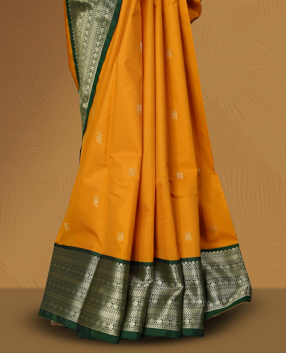 Mustard yellow colour soft silk saree adorned with golden buttas, highlighted by a rich green border and pallu with intricate zari designs & Paired with a matching blouse.