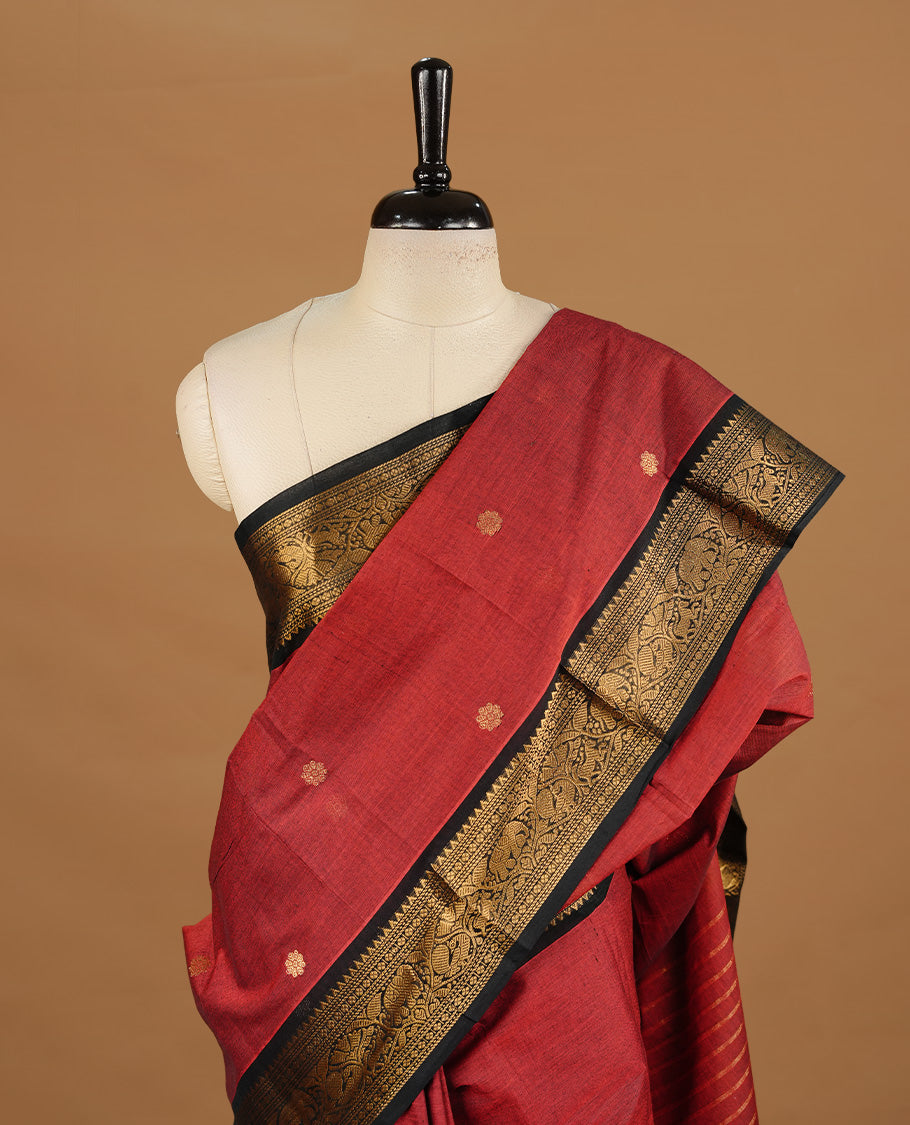 Dark red colour chettinad cotton saree featuring gold zari motifs on body, complemented by black colour with zari border, paired with matching blouse piece.