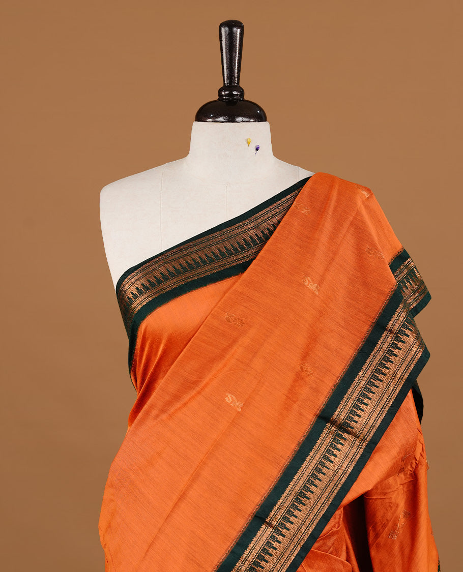 Orange colour kalyani cotton saree featuring gold zari motifs on body, highlighting contrast green colour with Antique gold zari border, paired with matching blouse piece.