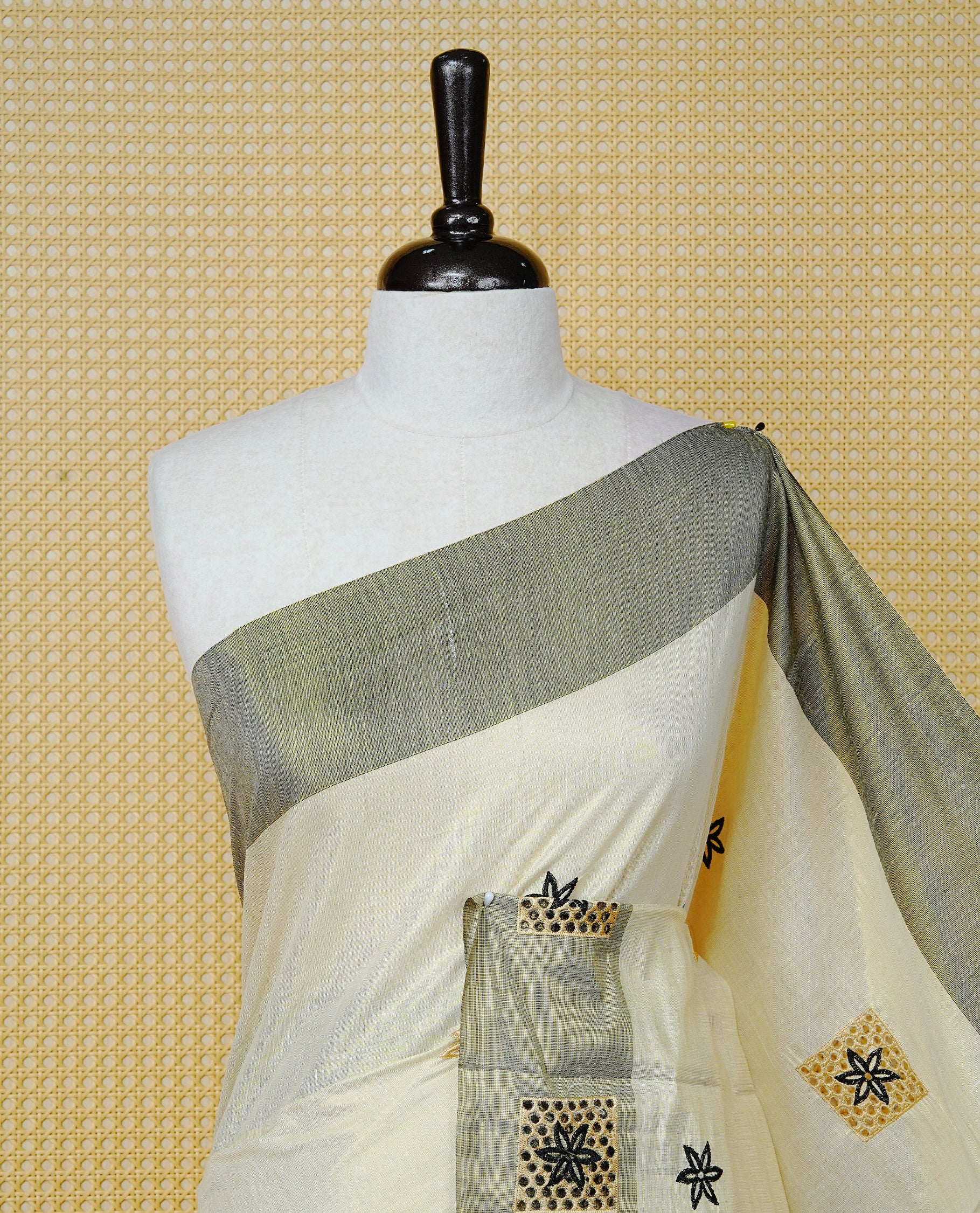 Cream Colour Tissue Kerala Saree Featuring Delicate Black Floral Embroidery Work Across The Body, Enhanced With A Grey Zari Border And A Rich  Black & Gold Zari Pallu, Finished With Black Tassels And A Matching Blouse Piece