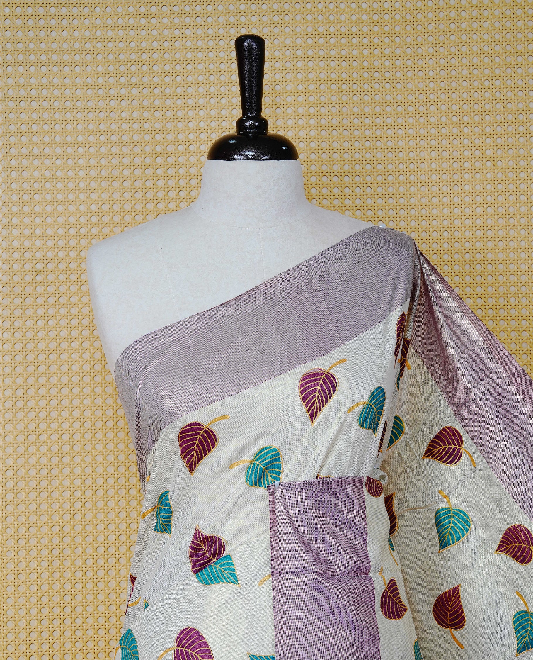 Cream Colour Tissue Kerala Saree Featuring Green and Brown Leaf Prints Across the Body, Enhanced with a Gold Zari, Purple and Green Border & Pallu, Green  and Purple  Tassels, and a Matching Blouse Piece.