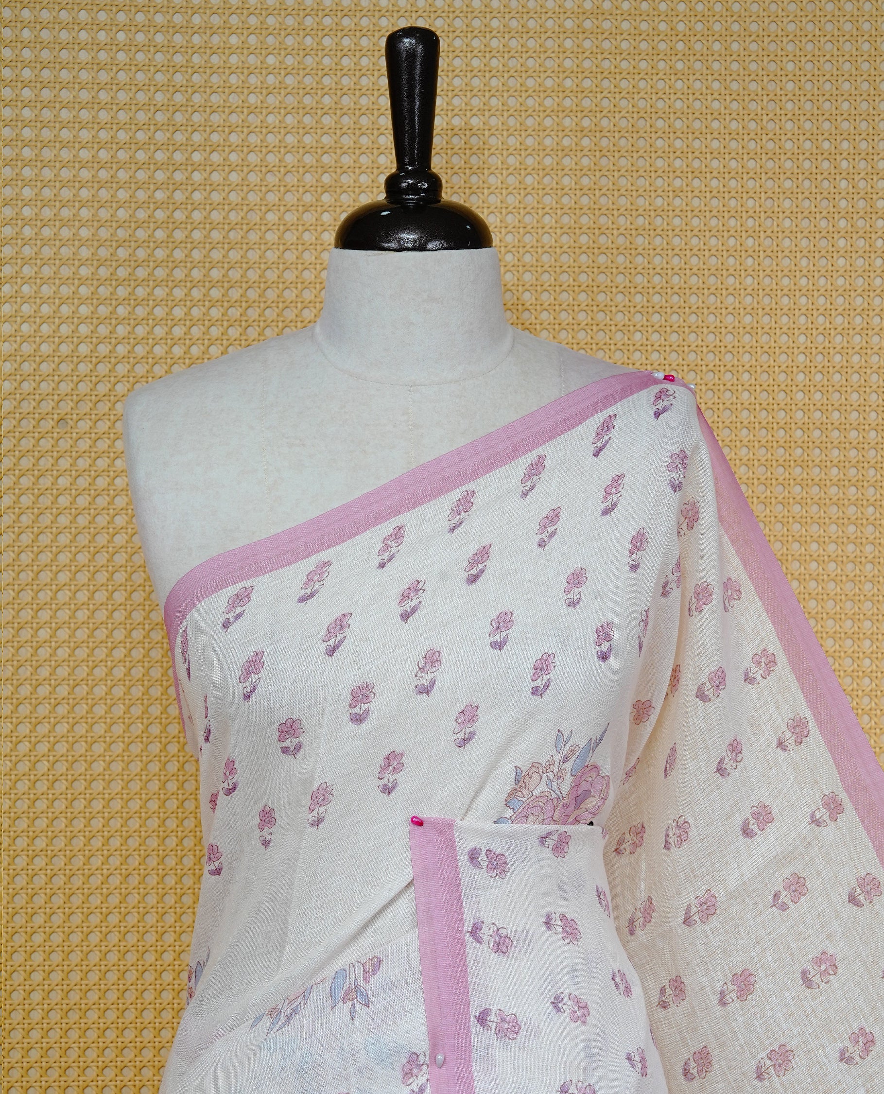 Cream colour semi linen saree featuring Floral printed buttas on body, complemented by contrast Pink colour border, comes with matching blouse piece.