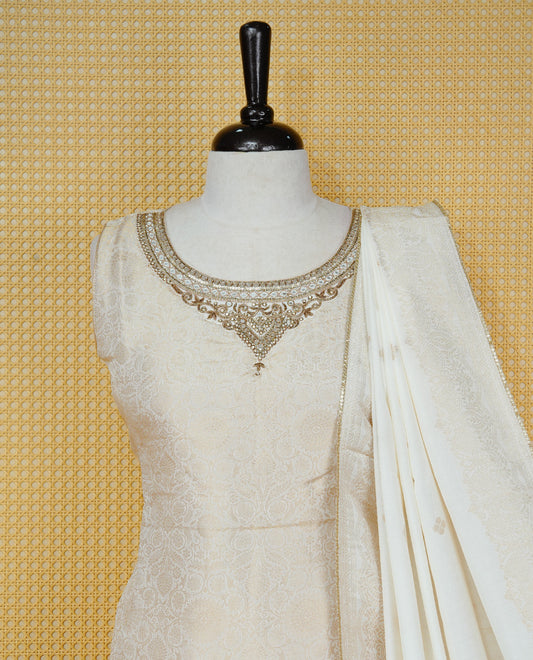 Cream colour churidar set featuring an all-over woven floral pattern and an intricately embellished neckline, paired with matching solid pants and a woven dupatta.