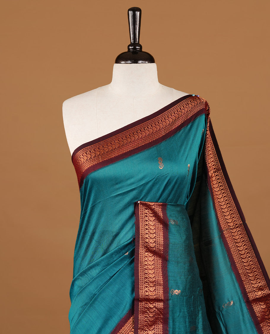 Teal green colour kalyani cotton saree featuring gold zari motifs on body, highlighting contrast Maroon colour with Antique gold zari border, paired with matching blouse piece.