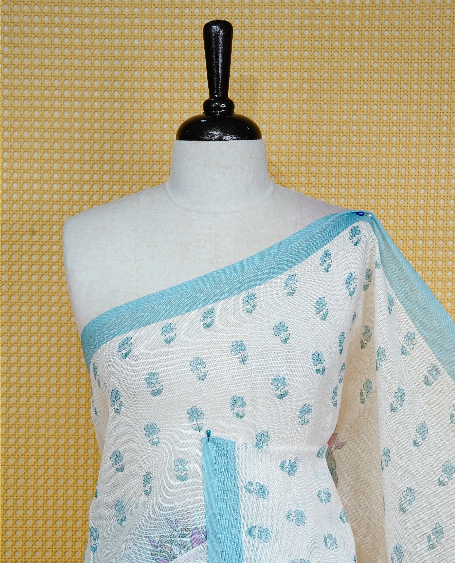 Cream colour semi linen saree featuring Floral printed buttas on body, complemented by contrast Blue colour border, comes with matching blouse piece.