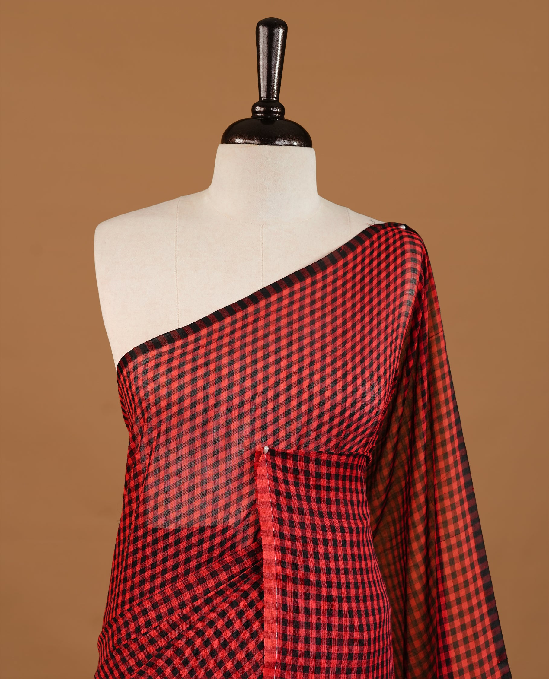 Red and Black colour Mul Cotton saree featuring a classic small check pattern on the body, accented with tassels for added charm. Comes without a blouse piece.