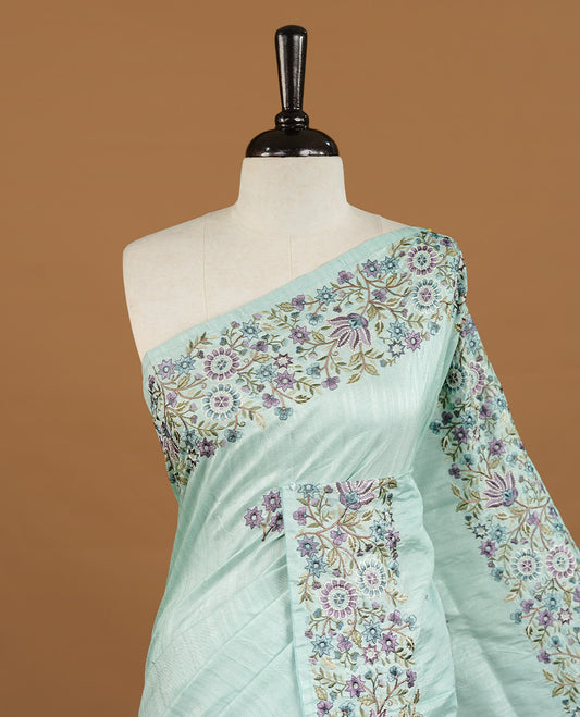 Mint colour Semi Tussar silk saree features an intricate, multi colored Kashmiri Kashida style floral embroidered border and scattered motifs, paired with a matching unstitched blouse piece.