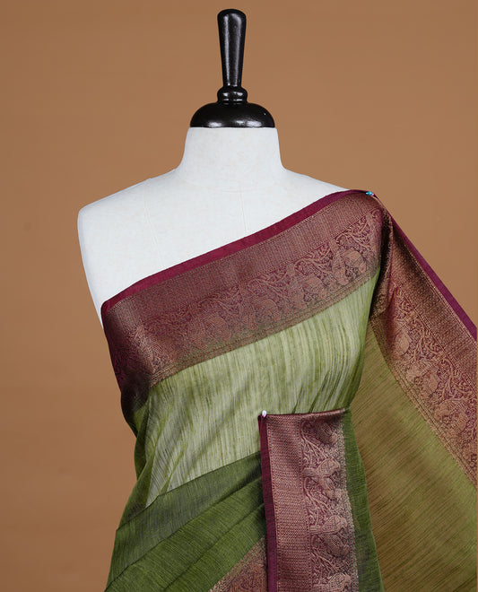 Olive green colour Semi linen saree featuring Elegant plain body, complemented by contrast Maroon colour With Antique zari border, paired with matching blouse piece.