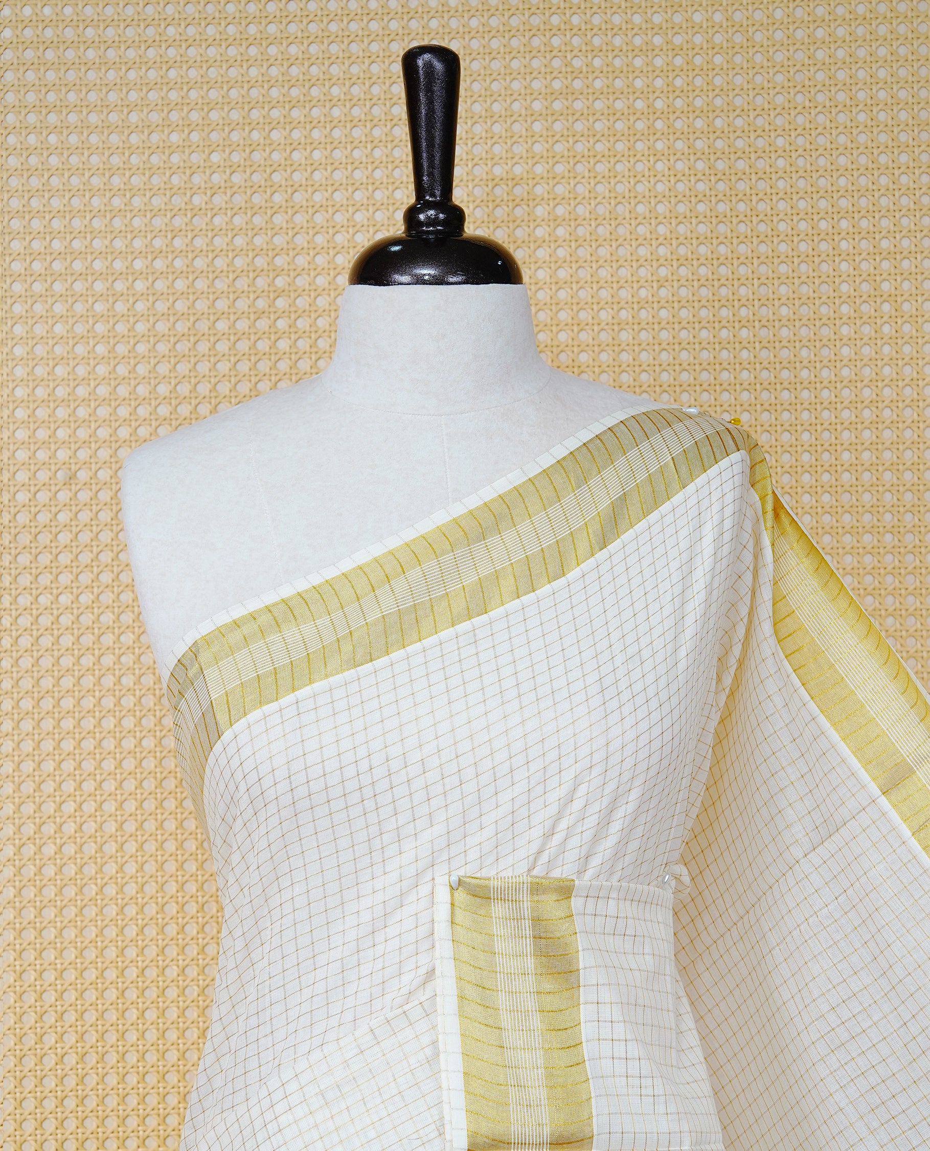 Cream Colour Cotton Kerala Saree Featuring A Golden Checks On Body, Enhanced With A Gold Zari  Border, A Traditional Gold Zari & Green Pallu, Green & Golden Tassels, And A Matching Blouse Piece.