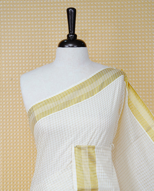 Cream Colour Cotton Kerala Saree Featuring A Golden Checks On Body, Enhanced With A Gold Zari  Border, A Traditional Gold Zari & Green Pallu, Green & Golden Tassels, And A Matching Blouse Piece.