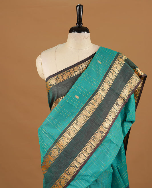 Teal colour chettinad cotton saree featuring gold zari motifs & check pattern on body, complemented by green colour with zari border, paired with matching blouse piece.