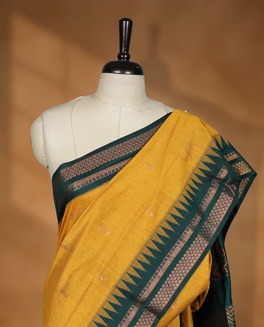 Mustard colour kalyani cotton saree featuring Antique zari motifs on body, contrast green colour border with geometric antique zari pattern, paired with matching blouse piece.