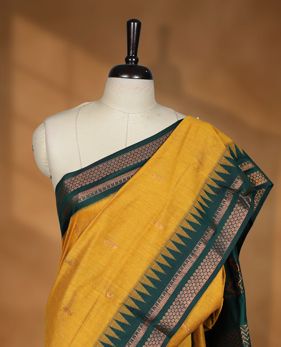 Mustard colour kalyani cotton saree featuring Antique zari motifs on body, contrast green colour border with geometric antique zari pattern, paired with matching blouse piece.