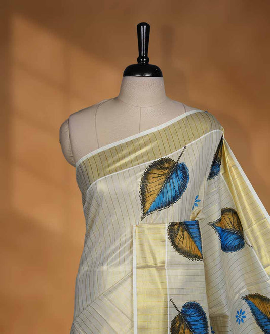 Off white colour Tissue Kerala saree featuring a subtle striped body with elegant blue and mustard leaf prints, complemented by a classic golden zari border and tasselled pallu, paired with a matching blouse.