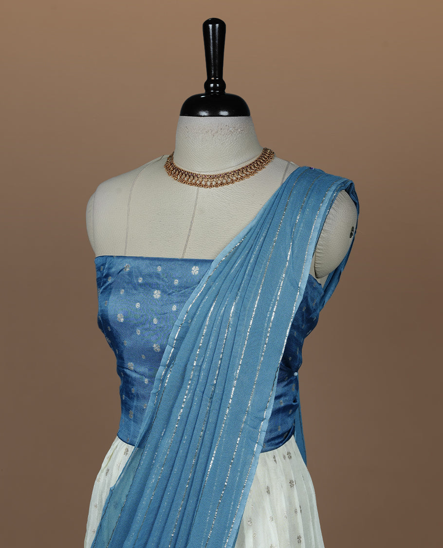 Off white semi banaras semi stitched dhavani set featuring gold zari motifs and contrast Bluecolour border, unstitched gold zari blouse piece and matching Duptta with gold zari stripes.