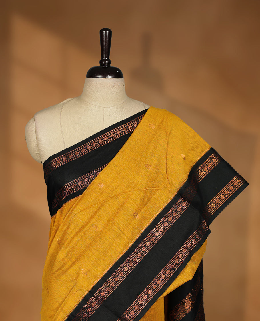 Mustard colour kalyani cotton saree featuring Antique zari motifs on body, contrast Black colour border with floral and chakra antique zari pattern, paired with matching blouse piece.