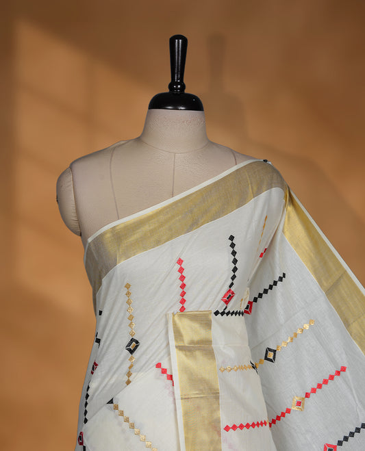 Off white Kerala saree featuring red and black geometric motifs, complemented by a classic golden zari border and traditional pallu, paired with a matching blouse.