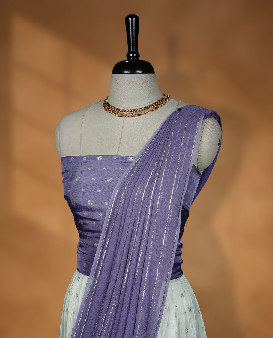 Off white semi banaras semi stitched dhavani set featuring gold zari motifs and contrast Lavender colour border, unstitched gold zari blouse piece and matching Duptta with gold zari stripes.