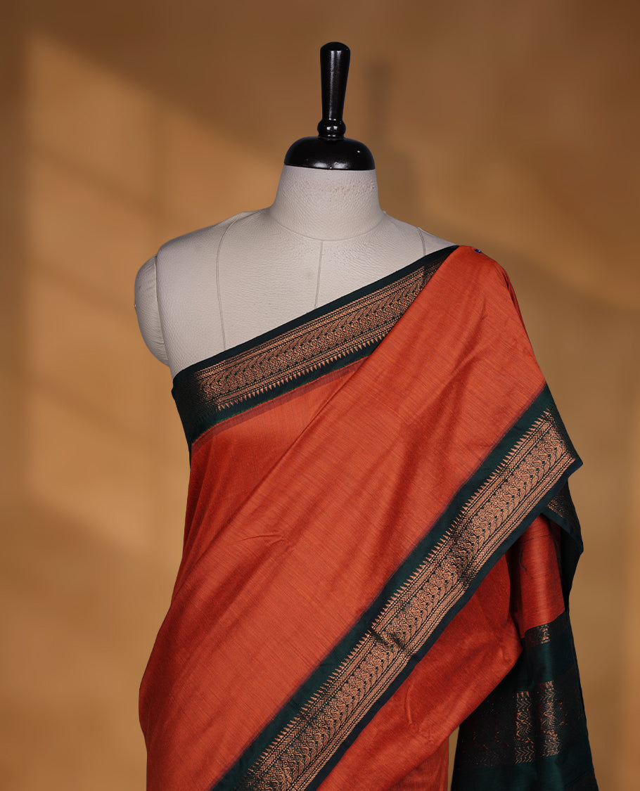 Rust orange colour Kalyani cotton saree featuring a plain elegant body, complemented by a rich dark green zari border and traditional woven pallu, paired with a matching blouse.