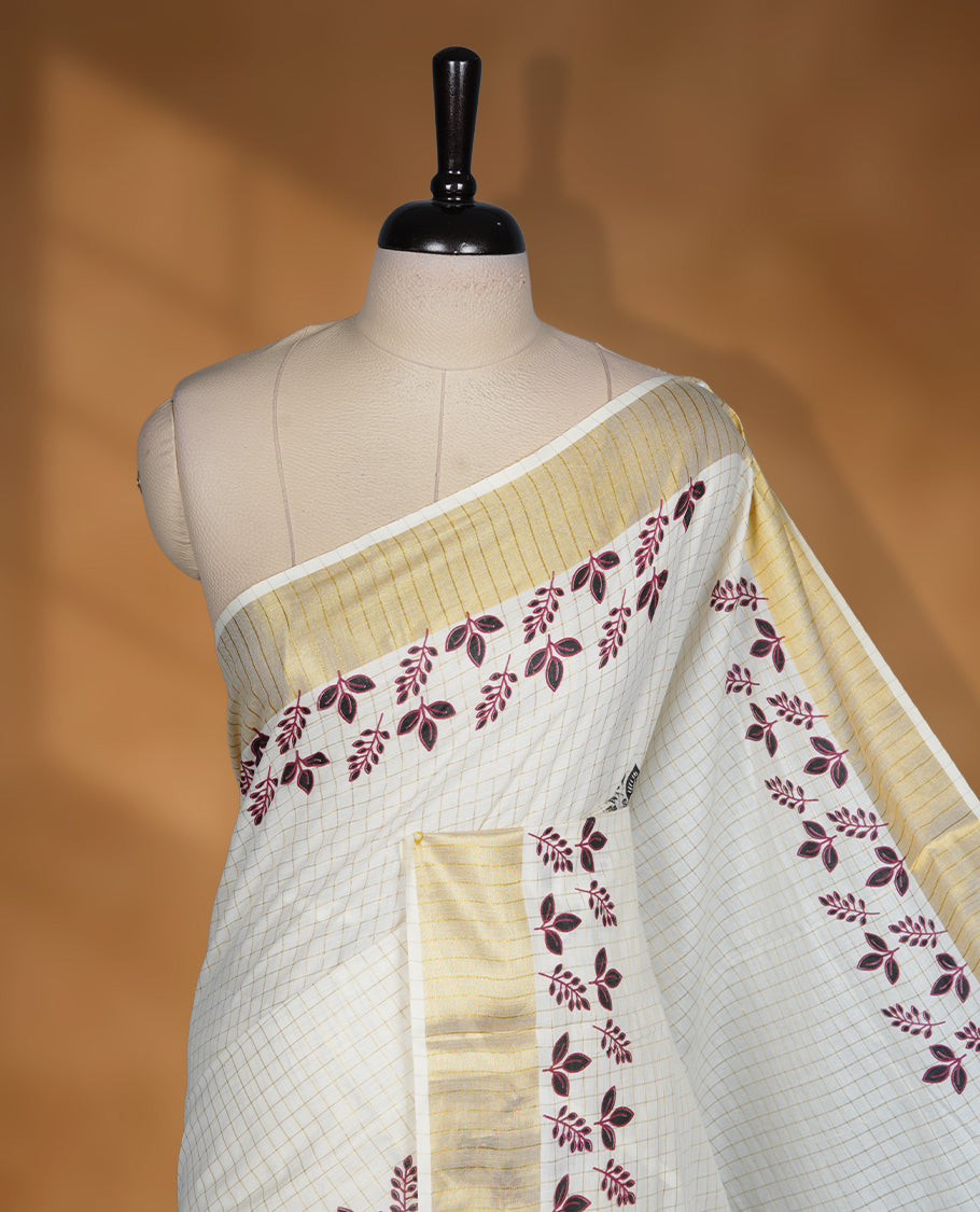 Off white colour cotton Kerala saree featuring a gold zari check pattern across body, a refined kasavu border with leaf print, paired with a matching blouse.