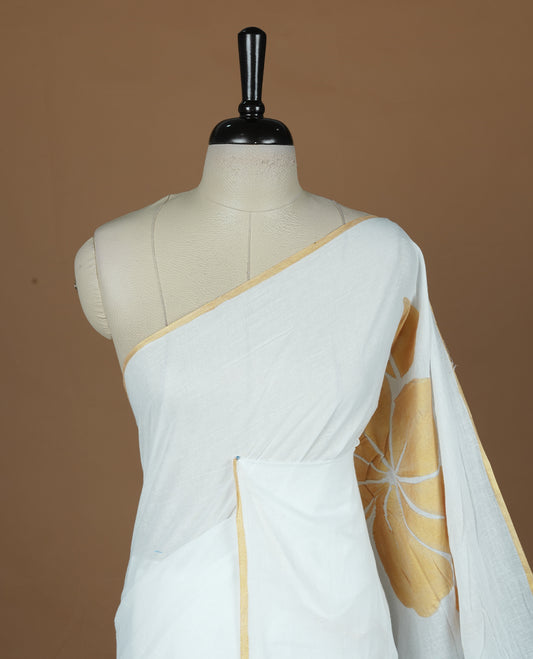 White coloured mul cotton saree featuring bold gold-tone floral motifs across the body, designed without a border and comes without a blouse piece.