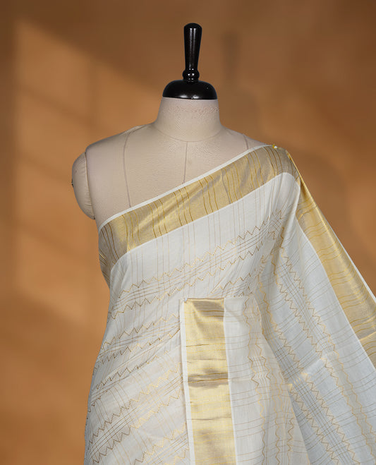 Off white Cotton Kerala saree featuring a subtle zari patterned body, complemented by a classic golden zari border and traditional pallu, paired with a matching blouse.