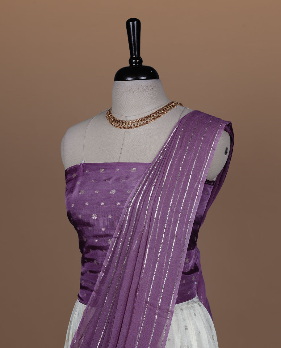 Off white semi banaras semi stitched dhavani set featuring gold zari motifs and contrast Purple colour border, unstitched gold zari blouse piece and matching Duptta with gold zari stripes.