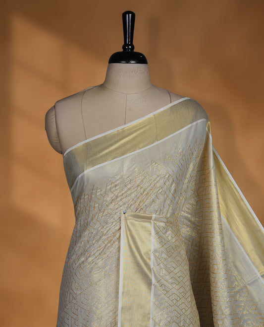 Off white colour Tissue Kerala saree featuring an elegant all-over zari patterned body, complemented by a rich golden zari border and traditional pallu, paired with a matching blouse.