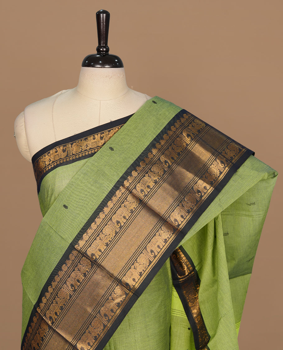 Green colour chettinad saree featuring gold zari motifs on body, complemented by contrast black colour with traditional border, paired with matching blouse piece.