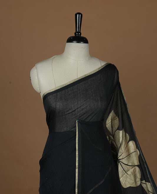 Black coloured mul cotton saree featuring bold gold-tone floral motifs across the body, designed without a border and comes without a blouse piece.