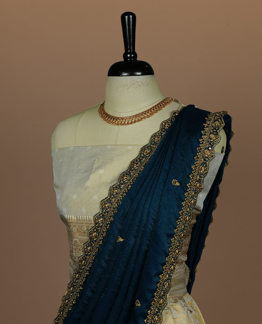 Light gold colour semi banaras semi stitched dhavani set featuring gold zari floral kodi motifs and traditional border, unstitched matching blouse piece and contrast Teal colour Duptta with gold thread and beats worked border.